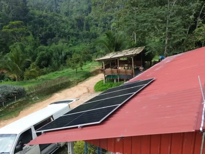Solar panels on the red metal roof of a farm building in a green hillside valley in Raub, Pahang